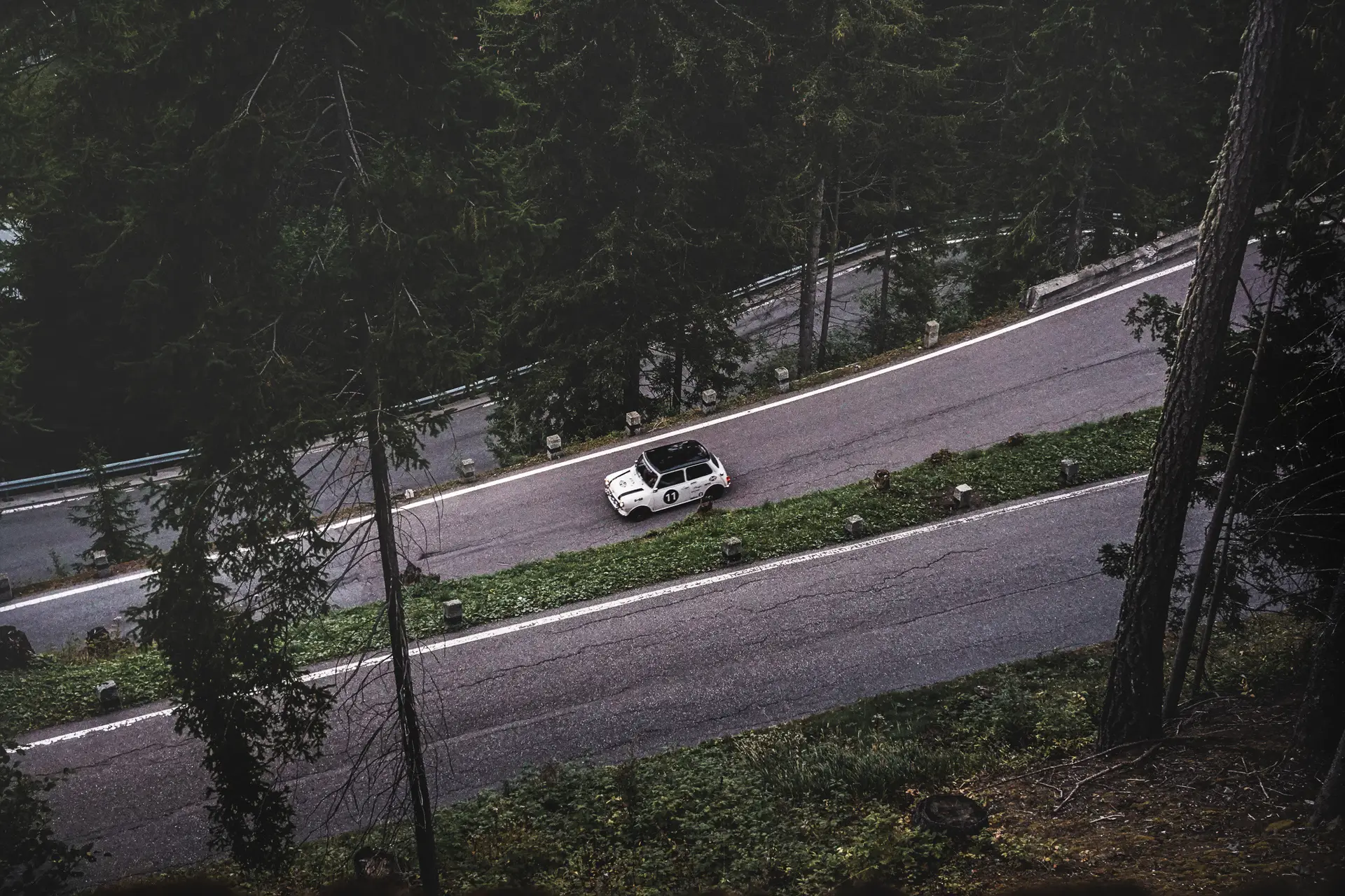 An image from far a above a Mini Cooper 998 Rally driving down on a road going down through many U-turns