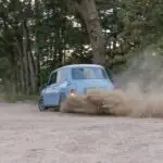 Een crossende lichtblauwe Austin Mini dat slipt in de bocht van een grindpad