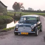 Een donkergroene Mini Cooper rijdend door de polders met links een houten stal