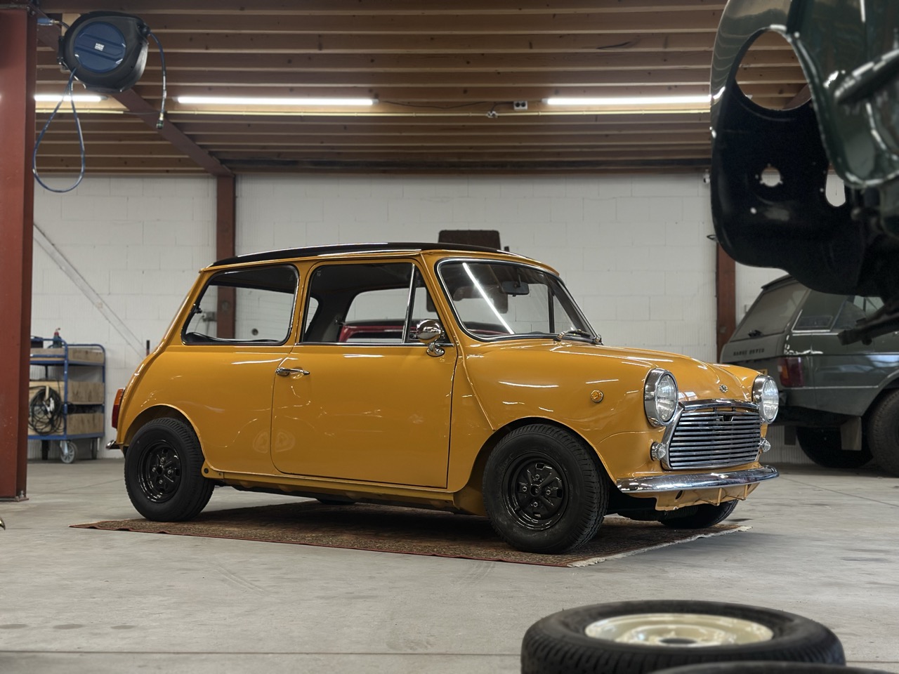 Innocenti mini cooper mk3 998cc in yellow fully restored standing in the workshop of brooks motors seen from the side
